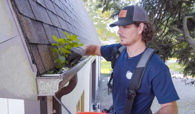 A Brothers Gutters crew member removing leaves from a rain gutter